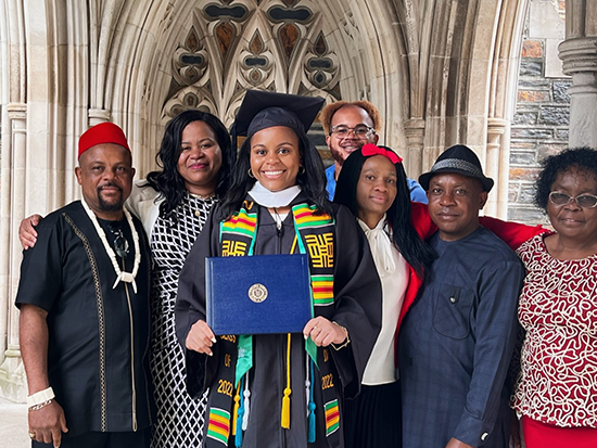 Natalie Ezem is shown smiling in a cap and gown, holding her diploma from Duke University while surrounded by her family.