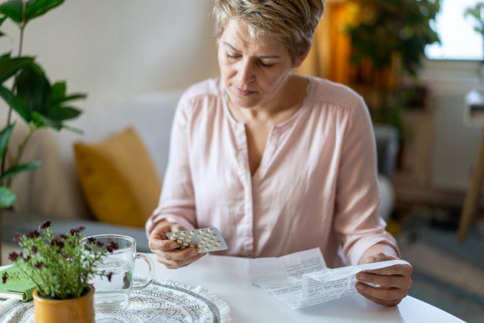 Woman sitting at table holding a blister pack of pills