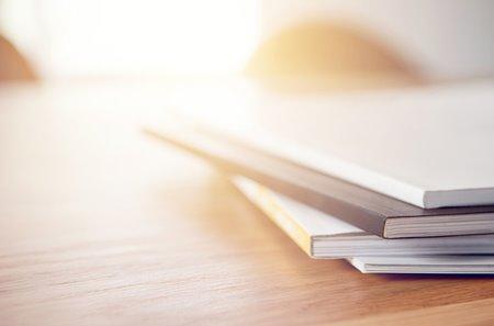 A pile of publications on a desk with a ray of sunshine coming in from behind.