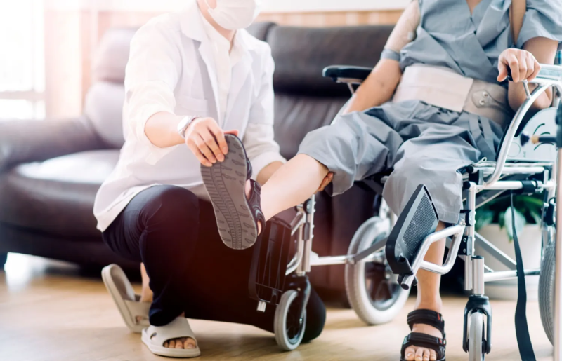 A caregiver helps a loved one in a wheelchair with foot flexing physical therapy exercises.