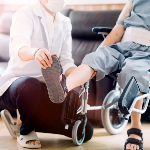 A caregiver helps a loved one in a wheelchair with foot flexing physical therapy exercises.