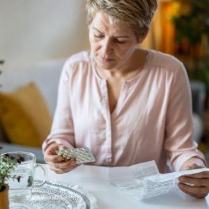 Woman sitting at table holding a blister pack of pills